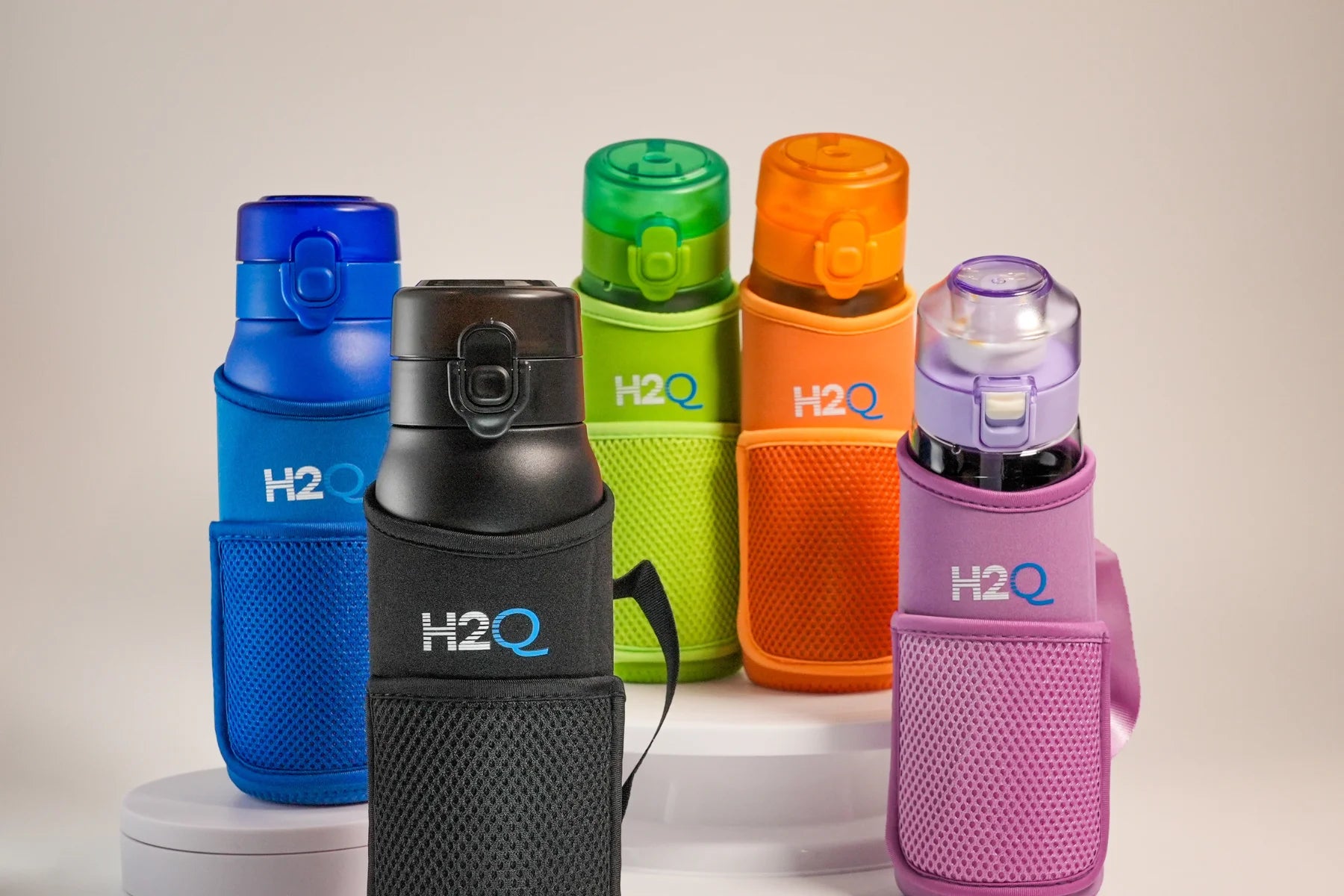 A collection of H2Q by SQOON Water Bottles (Black G3, Blue G3, Green G2, Orange G2 and Purple G1) with matching color Bottle Sleeves.